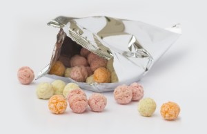 An opened aluminium bag of colorful sweet fruity flavor cereal balls on white background.